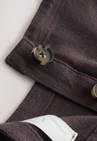 Close-up of dark brown fabric with stitched buttonholes and tortoiseshell-patterned buttons sewn on.