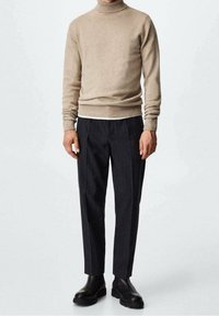 Pull à col roulé beige associé à un pantalon rayé sombre et des bottines Chelsea noires. Texture lisse avec un design ajusté, mettant en valeur une élégance décontractée.