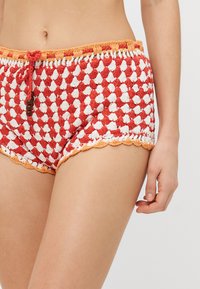 Gehaakte shorts in rood en wit met een geschulpte oranje rand. Heeft een trekkoord taille met houten kralen voor een verstelbare pasvorm.