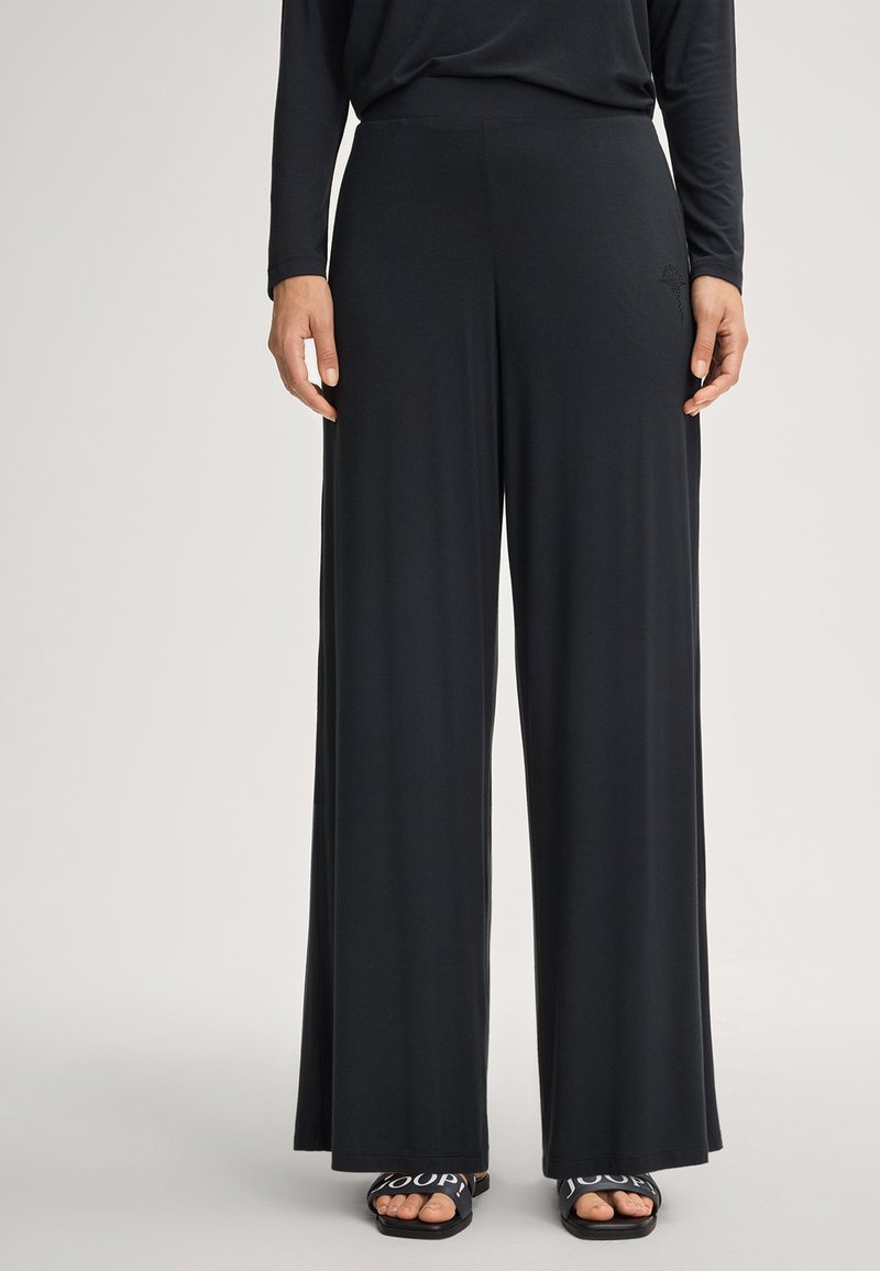 Schwarze weit geschnittene Hose aus weichem, leichtem Stoff, mit einem glatten Bund und einem dezenten Designdetail nahe der Hüfte.
