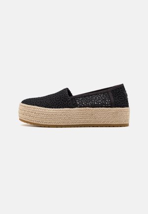 Chaussure noire slip-on en dentelle avec une semelle plateforme beige épaisse tissée et une semelle en caoutchouc, présentée de profil sur un fond uni.
