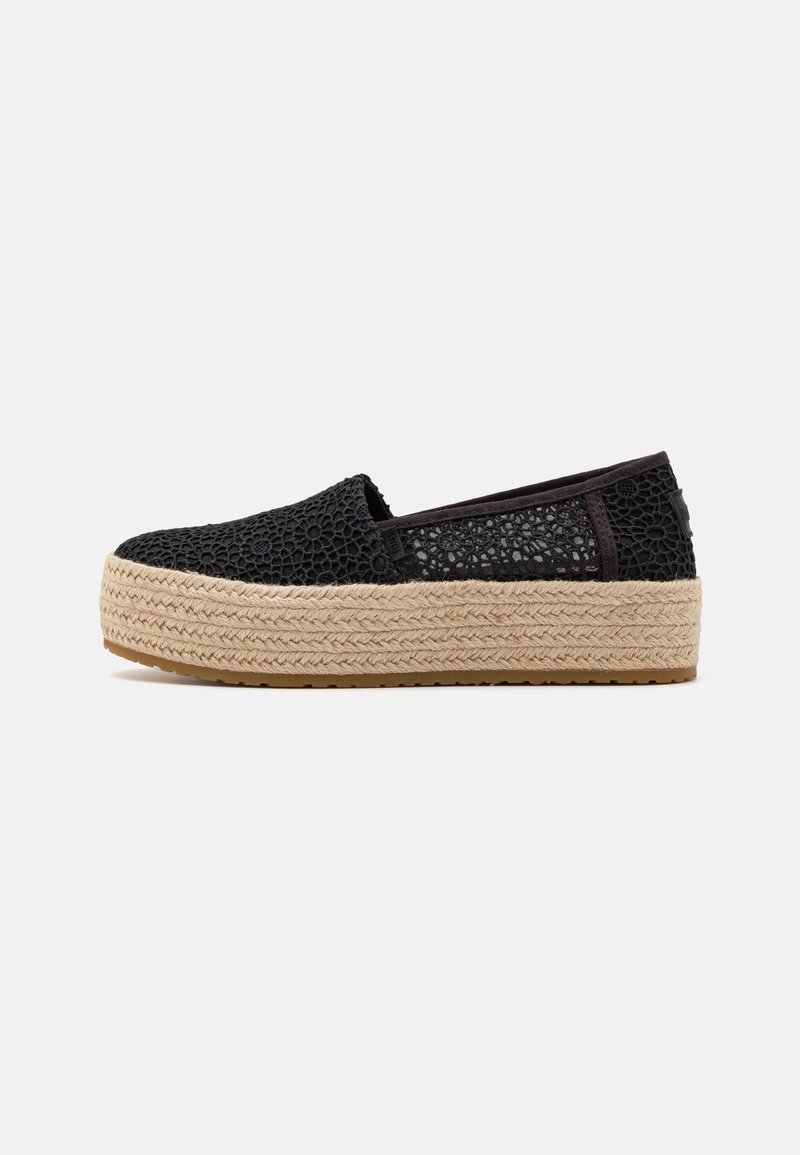 Chaussure noire slip-on en dentelle avec une semelle plateforme beige épaisse tissée et une semelle en caoutchouc, présentée de profil sur un fond uni.
