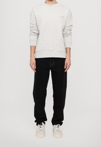 Felpa grigia chiara con polsini e vita a costine, caratterizzata da un piccolo logo ricamato "CLOSED". Abbinata a pantaloni neri e sneakers beige.