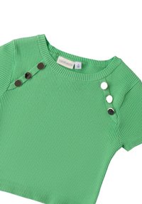 Top corto de manga corta verde con cuello redondo y botones decorativos en negro y metálico en un hombro. Textura suave y diseño ajustado.