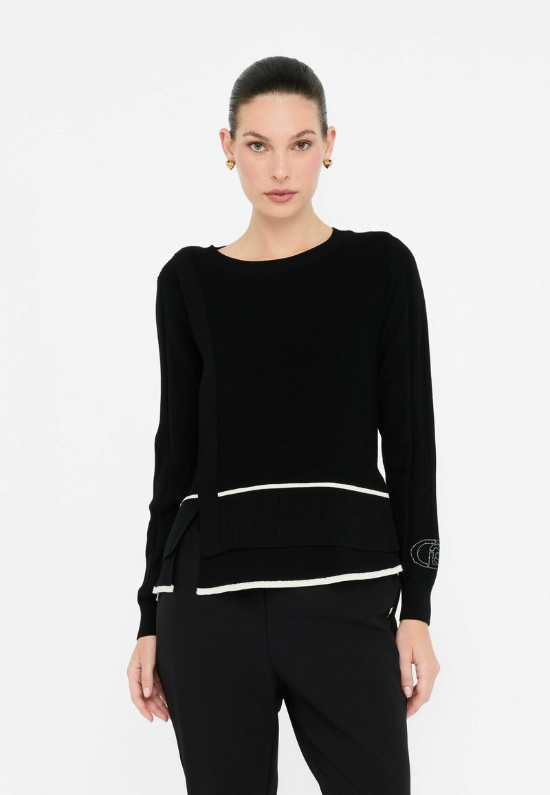 Maglione nero a maglia con scollatura rotonda, maniche lunghe e dettagli bianchi all'orlo. Presenta una fessura laterale e decorazioni su una manica.