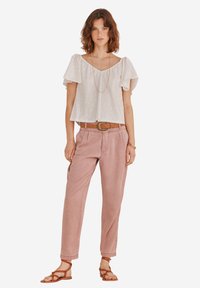 Weiße Baumwollbluse mit Rüschensäumen, kombiniert mit einer hellrosa lässigen Hose und braunen Ledersandalen. Einfaches Halskettenakzent.