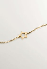 Pulsera de cadena dorada con un charm en forma de estrella con un centro abierto, que destaca por su diseño elegante y textura suave.