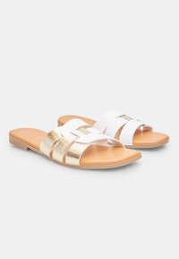Sandales à glissière blanches et dorées avec un bout ouvert, présentant de larges sangles et une semelle plate avec une finition texturée.