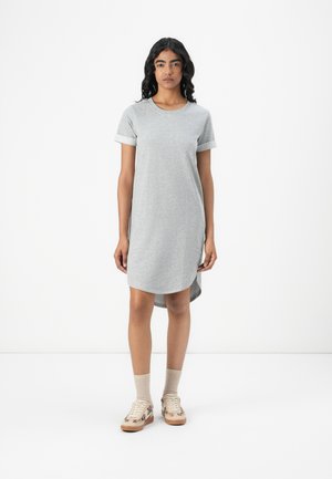 Robe t-shirt grise à manches courtes et ourlet arrondi, fabriquée en tissu doux, associée à des baskets beiges et des chaussettes à la cheville.