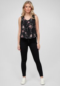 Must have sleeveless mustärikas bluus roosa lillemustriga, kombineerituna mustade kitsaste teksade ja valgete tossudega, näidates sobivat siluetti ja pehmet tekstuuri.