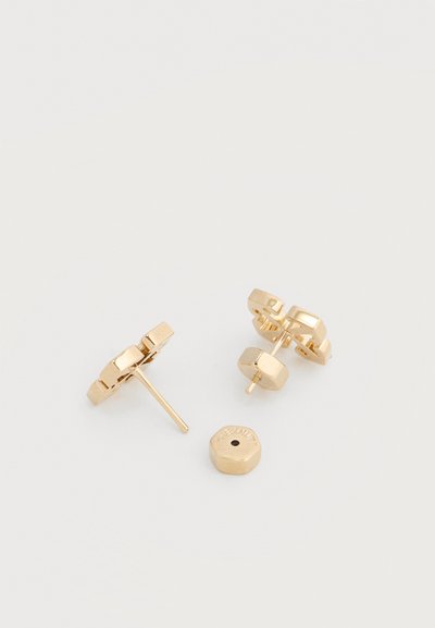 Ζευγάρι χρυσών μεταλλικών σκουλαρικιών καρφίτσες με εξαγωνικά σχήματα και ένα χαλαρό πίσω μέρος σκουλαρικιού σε λευκό φόντο.