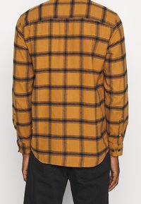 Chemise en flanelle à manches longues pour homme en jaune moutarde avec un motif à carreaux bleu marine. Dotée d'un ourlet droit, de poignets à boutons et d'une seule empiècement au dos.