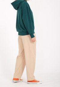 Teal hoodie med snøre, beige vide bukser og orange sneakers. Blødt stof, afslappet pasform og enkelt design uden mønstre.