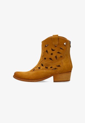 Beżowy zamszowy botek za kostkę z niskim, warstwowym obcasem, ozdobnymi wycięciami i zamkiem błyskawicznym z tyłu.