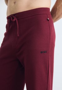 Bordeauxkleurige loungebroek van gestructureerde stof met een trekkoord in de taille en geborduurd "BOSS"-logo aan de zijkant.