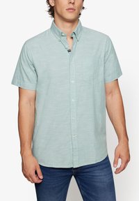 Camisa de botones de manga corta en verde menta claro, hecha de un tejido ligero. Presenta un bolsillo en el pecho y un cuello clásico con detalles de botones.
