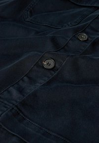 Donkerblauwe button-up shirt gemaakt van glad, geweven stof, met knopen aan de voorkant en een zak, en zichtbare stiksels.