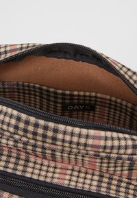 Beige ja ruskeanruudullisen laukun sisäosa, jossa on sileä, teksturoidulla vuorauksella. Vetoketjusuljin mustalla reunuksella, sisätilassa näkyy merkki.