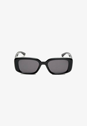 Lunettes de soleil noires rectangulaires avec des verres foncés, monture en plastique lisse et branches courbées. Le design est épais avec une esthétique minimaliste.