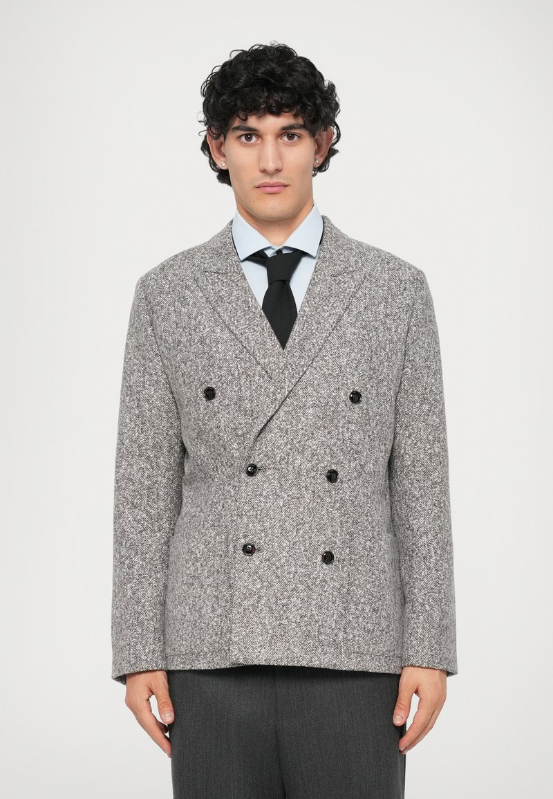 Grå hørflet dobbeltbrystet blazer med sorte knapper, klippet krave, tekstureret stof og sidelommer; parret med en lyseblå skjorte og slips.