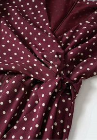 Gros plan sur un tissu bordeaux à pois blancs noué, montrant la texture et les plis sur un matériau lisse.