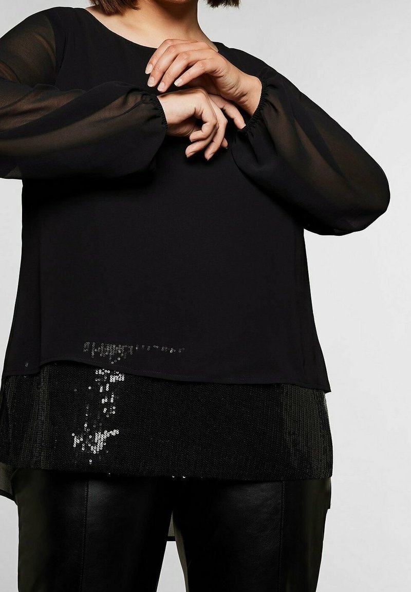 Blusa nera con maniche lunghe trasparenti e bordo inferiore decorato con paillettes. Tessuto morbido, taglio rilassato, abbinabile a pantaloni in pelle nera.