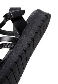 Sandalo nero con suola in gomma texture e cinturini in pelle intrecciata. Presenta una fibbia regolabile alla caviglia per una vestibilità sicura.
