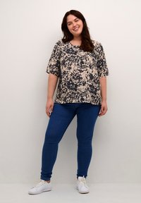 Haut à motif floral en beige et marine, manches courtes, coupe décontractée, associé à un jean skinny bleu et des baskets blanches. Design simple et texturé.