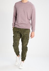 Jasnofioletowa koszula z długim rękawem i prążkowanymi krawędziami, zestawiona z oliwkowo-zielonymi spodniami cargo w kamuflażu oraz białymi tenisówkami. Swobodny krój i luźny styl.