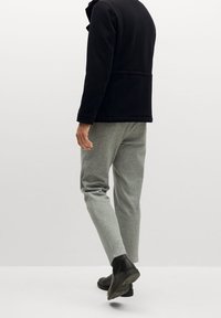 Musta fleece-takki, vaaleanharmaat tekstuuripöksyt ja mustat nilkkakengät. Puhtaat linjat, rento istuvuus ja ei näkyviä koristeita.