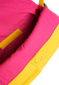 Gelbe Lederhandtasche mit leuchtend rosa Innenfutter. Verfügt über ein gesticktes Etikett "Antoine & Lili" aus gelbem Leder. Abgerundete Form, glatte Textur.
