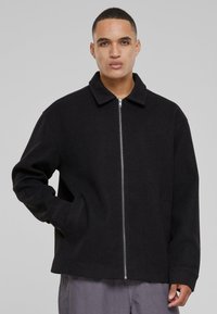 Black wool-blend jacket with a zip front, point collar, and side pockets; features a relaxed, slightly oversized fit and smooth texture.