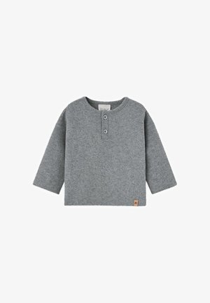 Chemise grise à manches longues en tissu doux, avec un col rond, une fermeture à trois boutons et une petite étiquette de marque en bas à gauche.