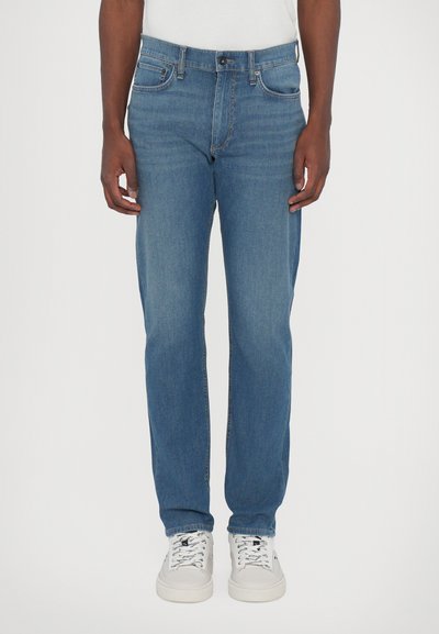 Hellblaue Denim-Jeans mit geradem Schnitt, Fünf-Taschen-Design und Kontrastnähten. Kombiniert mit weißen Sneakers für einen lässigen Look.