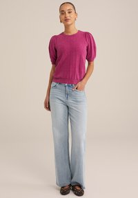 Maglione a maglia strutturata fucsia con maniche a sbuffo, abbinato a jeans in denim blu chiaro a gamba larga e scarpe nere con borchie dorate.