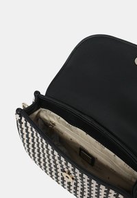 Borsa a tracolla tessuta in bianco e nero con un interno nero liscio. Presenta una chiusura in metallo dorato e scomparti interni multipli.