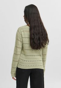 Ljusgrön stickad tröja med horisontella randmönster och små utskärningar. Långa ärmar och ribbade muddar. Avslappnad passform.