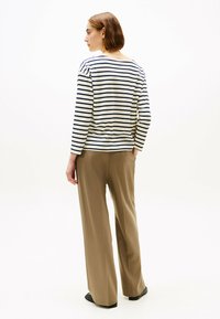 Maglietta a maniche lunghe a righe in crema e blu navy, abbinata a pantaloni leggeri a gamba larga color sabbia. Tessuto liscio, vestibilità casual, scollatura posteriore sottile.