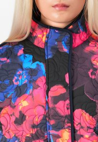 Quilted jacket featuring a black background with vibrant pink, blue, and orange floral patterns, high collar, and contrasting stitching details.