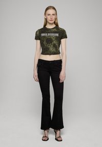 Zkrácené zelené tričko s leopardím potiskem a nápisem "True Religion", doplněné černými zvonovými džíny a černými páskovými podpatky.