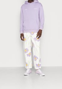 Felpa lilla con testo "Faded", pantaloni bianchi con motivi floreali viola e sneakers lilla coordinate. Vestibilità casual, materiali comodi.