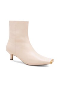 Krēmkrāsas ādas potītes zābaki ar smailu purngalu, zemu kaķēnu papēdi un zelta metāla purngala detaļu. Gluda tekstūra un bezvīļu dizains.