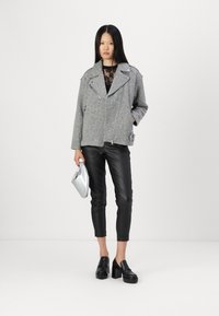 Veste de motard en laine grise mélangée avec fermeture éclair asymétrique, pantalon en cuir noir et pochette métallique argentée, associée à des mocassins à plateforme noirs.