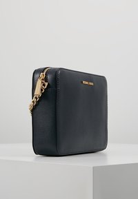 Černá kožená crossbody taška se strukturovaným obdélníkovým tvarem, zlatým řetízkovým popruhem a zipem, s logem na přední straně.