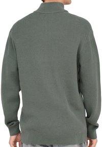 Maglione verde a coste con colletto alto, maniche lunghe e vestibilità rilassata. Presenta una texture che enfatizza calore e comfort.
