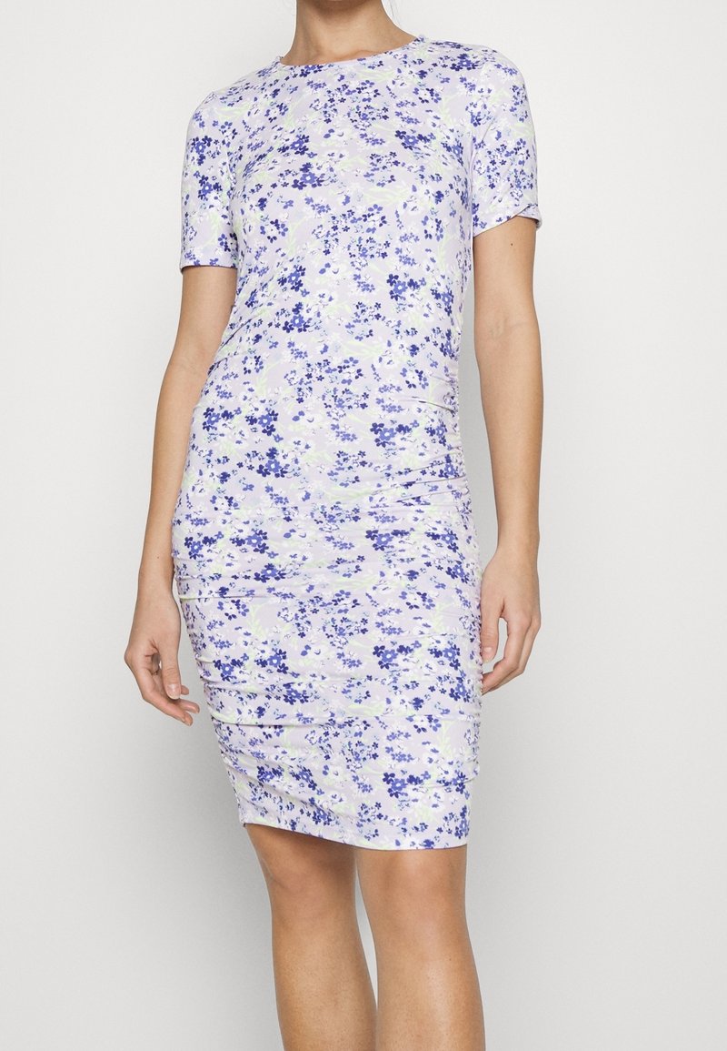 Krótkiej sukienki w kwiaty z lekkiego materiału; ma liliową bazę z fioletowymi i zielonymi kwiatami, krótkie rękawy oraz dopasowany krój.