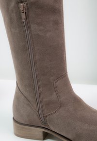 Botte haute en daim marron avec fermeture éclair latérale, surface texturée et petit talon bloc.