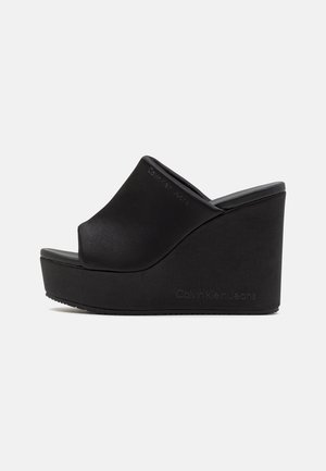 Sandales à talon noir en matériau lisse avec un design à bout ouvert. Présente une silhouette élégante et un détail embossé "Calvin Klein Jeans".