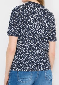 Femme portant une chemise à manches courtes noire et blanche à motifs, avec un jean en denim bleu, vue de dos.