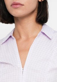 Ανοιχτό λεβαντίνη πουκάμισο με γιακά και μικρό καρό μοτίβο, με πατιλέτα και απαλό ύφασμα. Κοντινό πλάνο στη γραμμή του λαιμού και το γιακά.